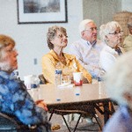 Men and women are seated and directing their attention to the front